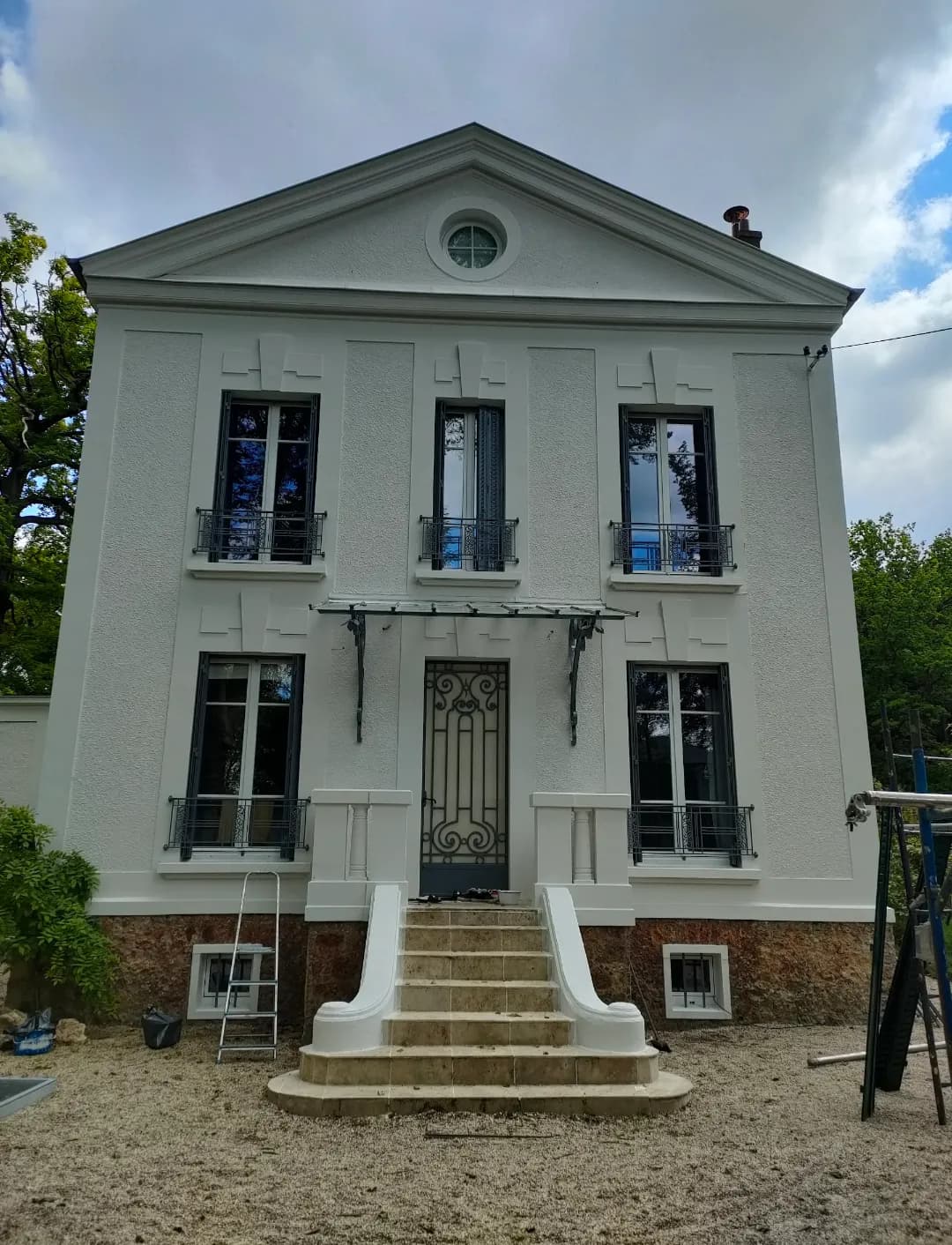 Façade blanche d’une maison bourgeoise à fronton et oculus, garde-corps en fer forgé, après l’intervention d’Artisans L.L